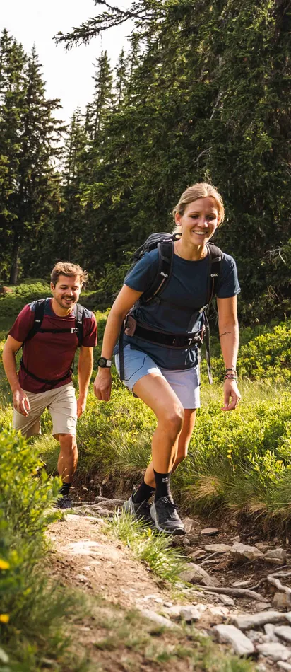 Lächelnde Wanderer auf einem üppig grünen Bergwaldpfad bergauf unterwegs