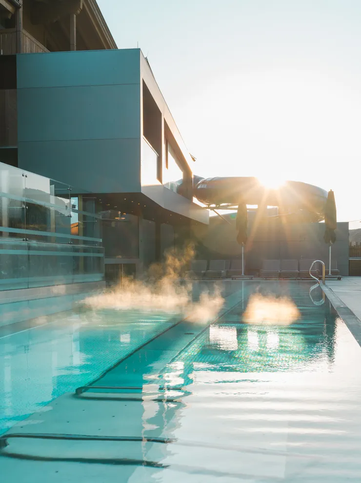 Dampf steigt aus beheiztem Außenpool eines modernen Hotels bei Sonnenaufgang auf