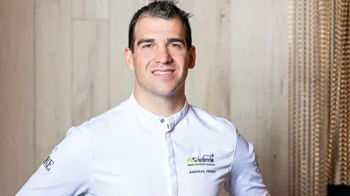 Smiling chef in white uniform standing in front of wooden wall
