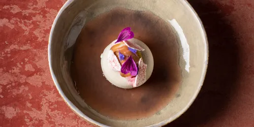 Gourmet-Dessert mit essbaren Blüten in einer Keramikschale auf roter Strukturfläche serviert