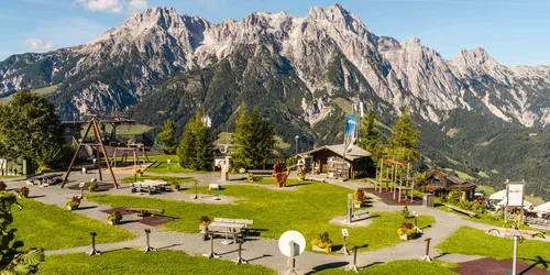 Alpiner Spielplatz mit Holzausstattung vor Bergkulisse im Sommer