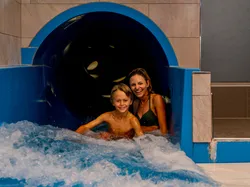 Lächelnde Mutter und Sohn kommen aus der Indoor-Wasserrutsche ins Becken