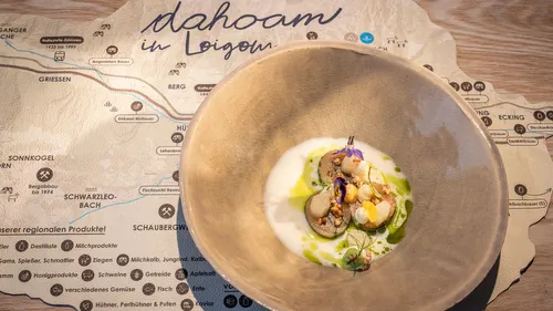 Gourmet plated dish with vegetables, sauce, and edible flowers on a rustic map-themed placemat