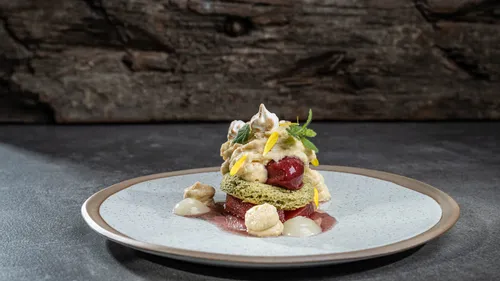 Gourmet-Dessert mit Biskuit, Kirsche, Creme und essbaren Blüten auf Keramikteller