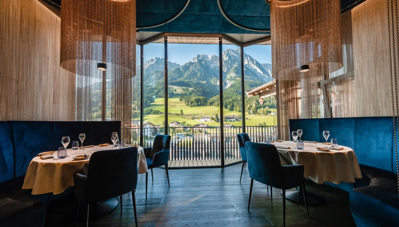 Modernes Restaurant mit Blick auf grüne Alpenwiesen und Berglandschaft durch Panoramafenster