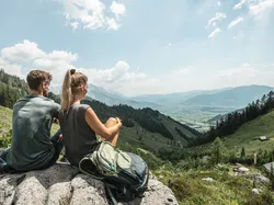 Hikers resting on a rock with a panoramic view of alpine valley and mountains