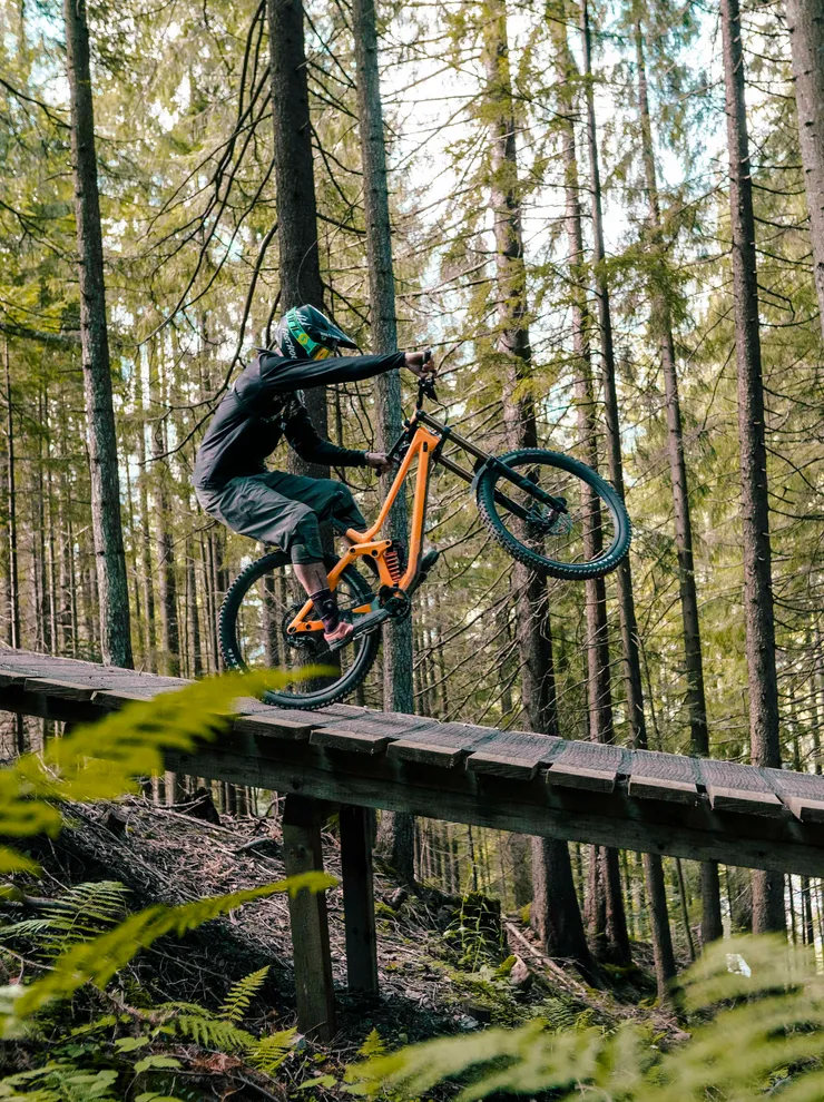 Mountain biker doing a wheelie on wooden trail ramp in forest