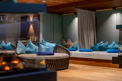 Moderner Spa-Loungebereich mit runden Korbsesseln, blauen Kissen und Kaminbeleuchtung