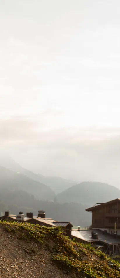 Mountain biker in pink gear doing a jump on dirt trail at sunset near alpine village