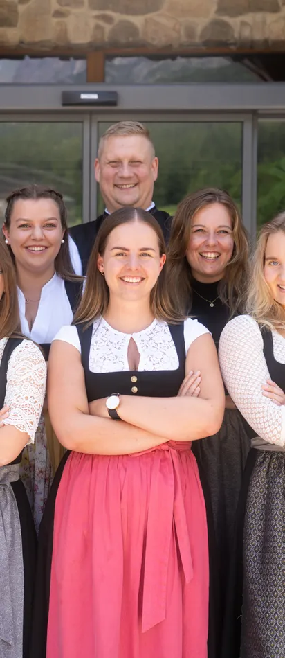 Team in traditioneller Tracht vor dem Hoteleingang lächelt in die Kamera
