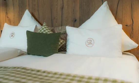 Cozy hotel bed with white pillows, green cushions and wooden headboard
