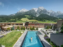 Bergresort mit Außenpool, Sonnenliegen und alpiner Landschaft im Hintergrund