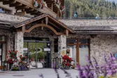 Eingang eines alpinen Hotels mit Holzfassade, Blumen und Blick auf Seilbahn im Hintergrund