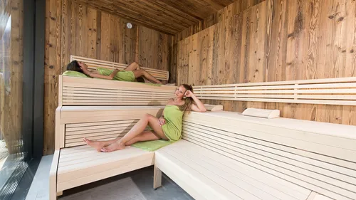 Women relaxing on wooden benches in modern sauna with towel wraps
