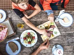 Kinder essen traditionelle Jause mit Wurst, Käse und Brot an einem Holztisch