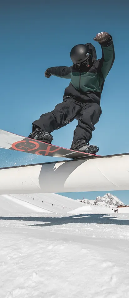 Snowboarder performing a rail slide trick in a sunny terrain park
