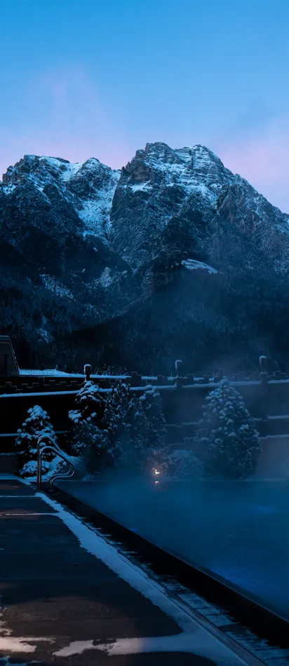 Heated outdoor pool in snowy mountain resort at dusk with scenic alpine backdrop