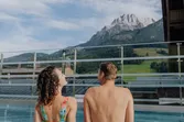 Paar in Badebekleidung entspannt am Pool mit Bergblick im Sommer