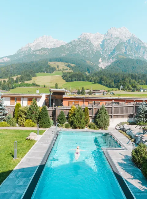 Außenpool mit Liegestühlen vor Alpenkulisse in sonniger Hotelanlage