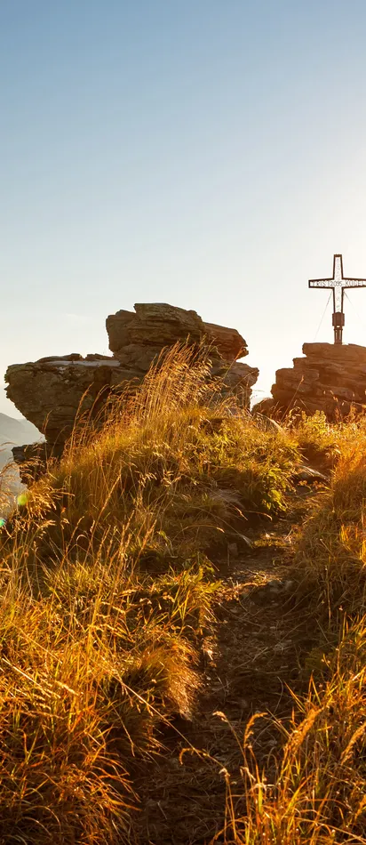 Mountain summit with peak cross at sunrise overlooking alpine landscape