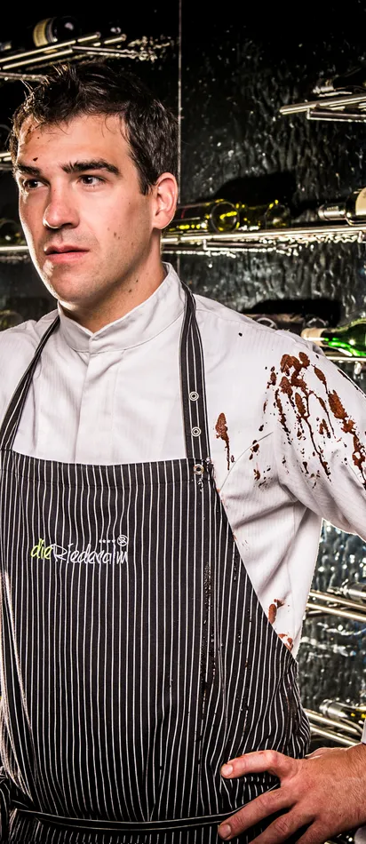 Pastry chef holding pot of melted chocolate with stained uniform in wine cellar
