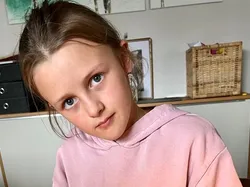 Mädchen färbt Osterei mit rotem Farbbad an Holztisch