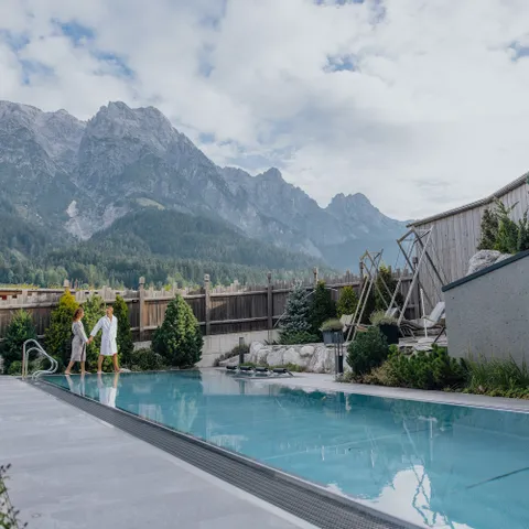 Couple walking by outdoor wellness pool with mountain view at luxury alpine resort