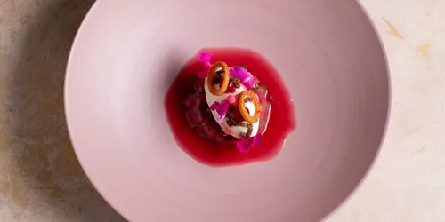 Gourmet-Dessert mit Sahne, essbaren Blüten und Beerensauce in rosa Schale